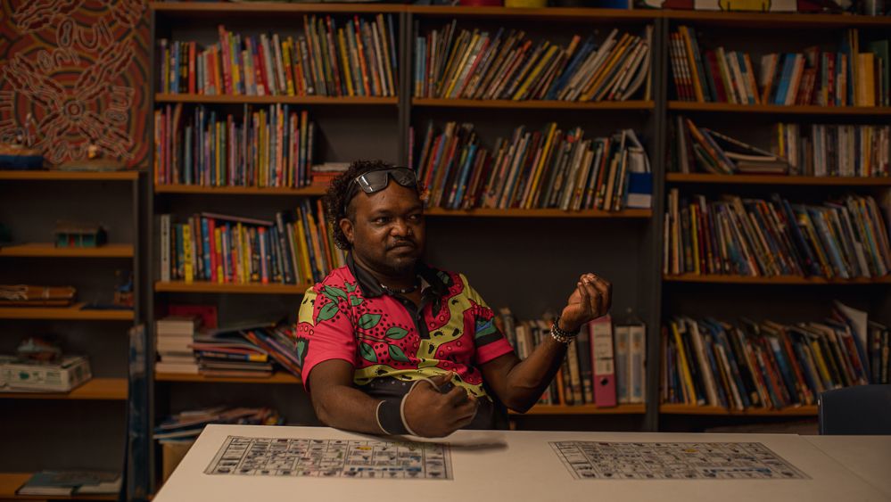 An Aboriginal man sitting in a library, speaking.