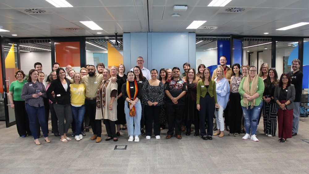 A large group of people standing in a conference room. They are Reconciliation Australia staff and participants at a RAP Learning Circle.