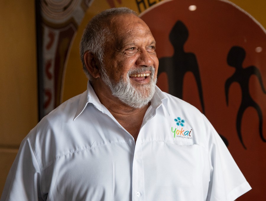An older Aboriginal man, smiling, wearing a shirt with a logo and the word 'Yokai' above the breast pocket.