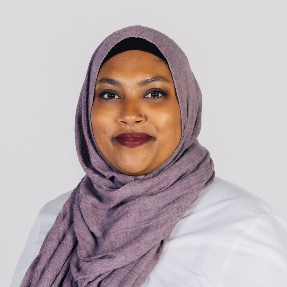 Rana Hussain - younger woman, brown skin, smart-casual attire, wearing a headscarf - standing in front of a light backdrop.