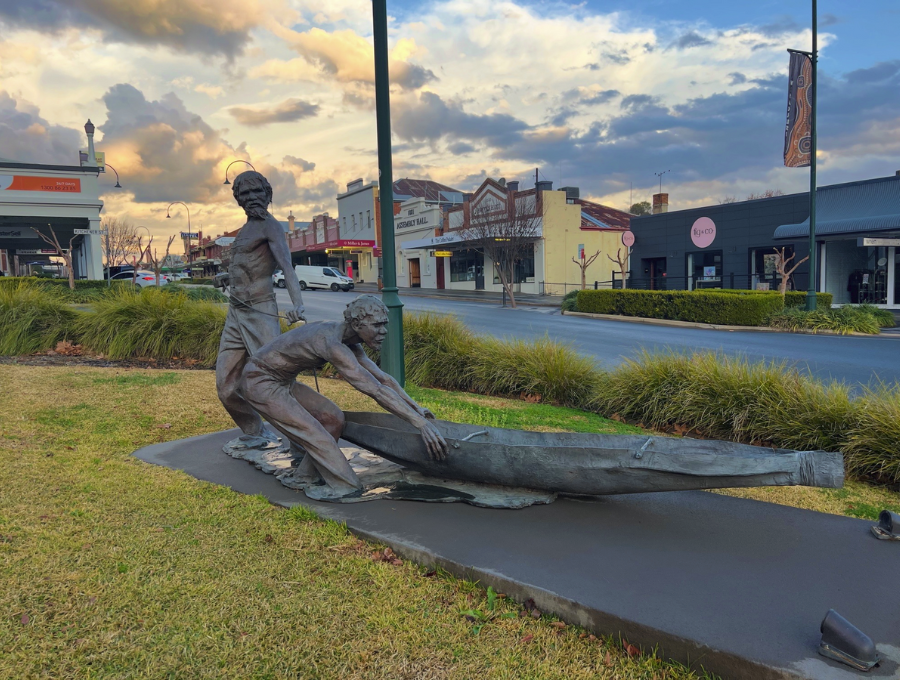 A bronze sculpture of two Aboriginal men pushing out a canoe.